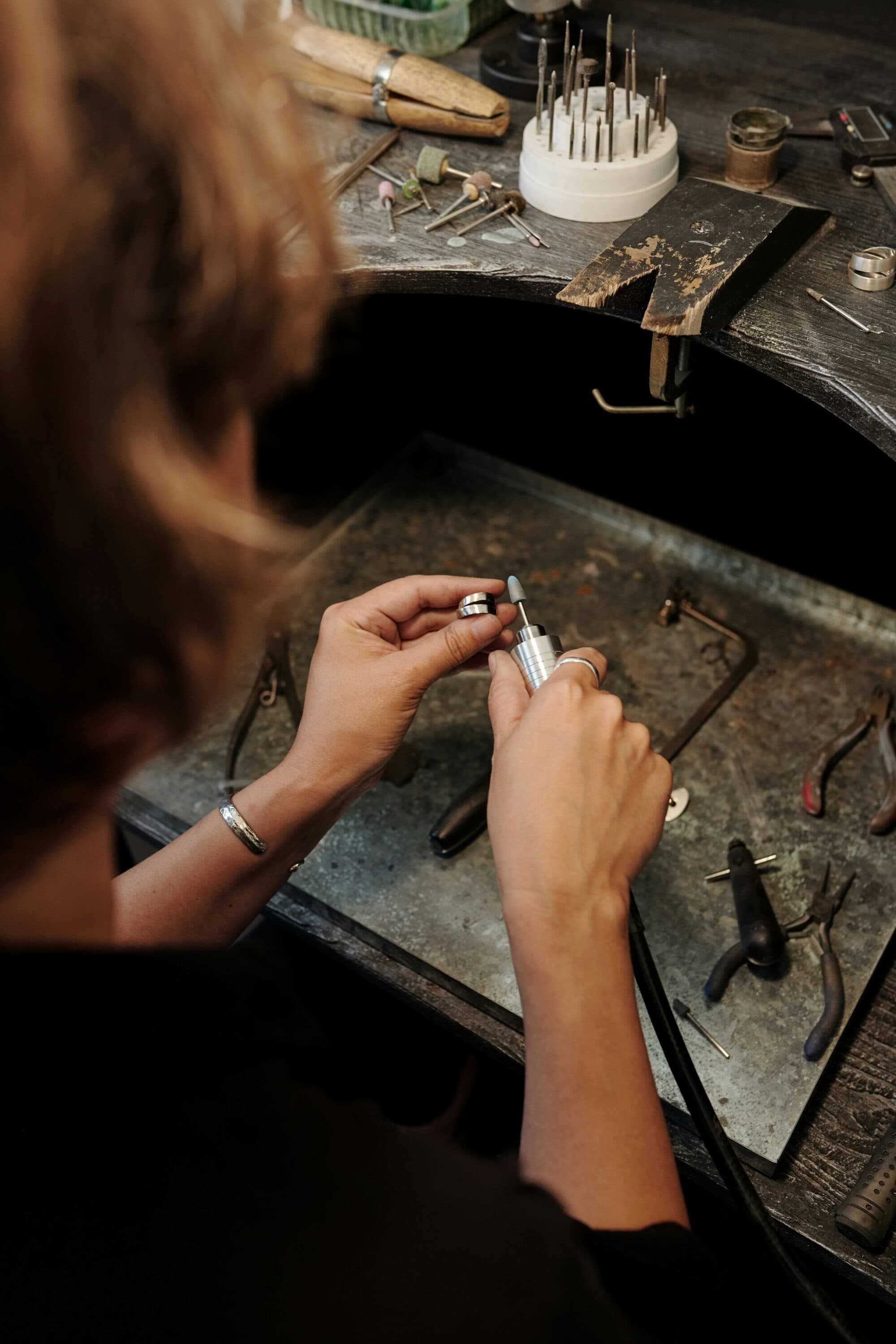 Bijoutier polissant une bague métallique avec un micro-moteur sur son établi