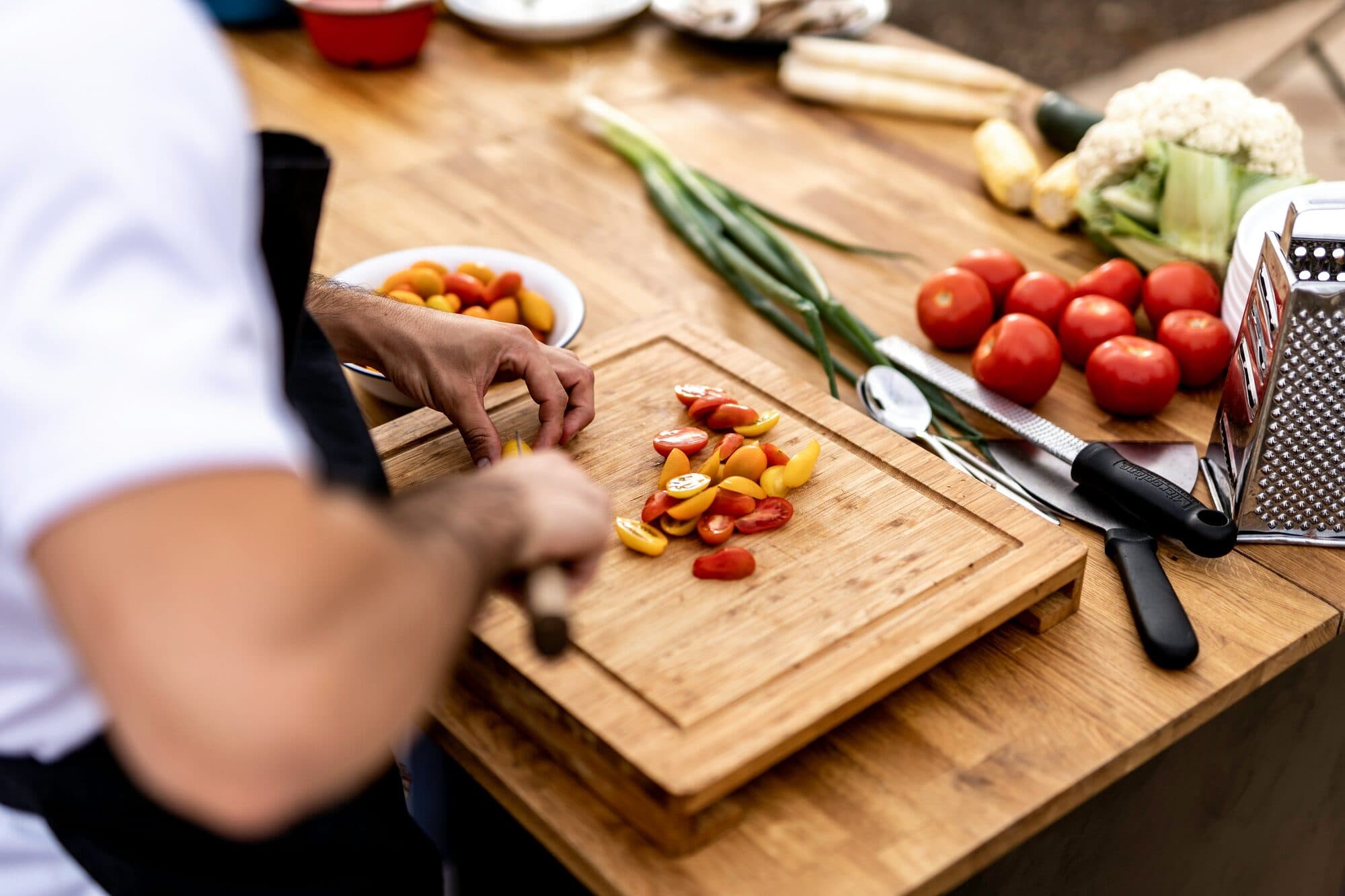 Mains tranchant des tomates cerises sur une planche en bois entourée de légumes frais
