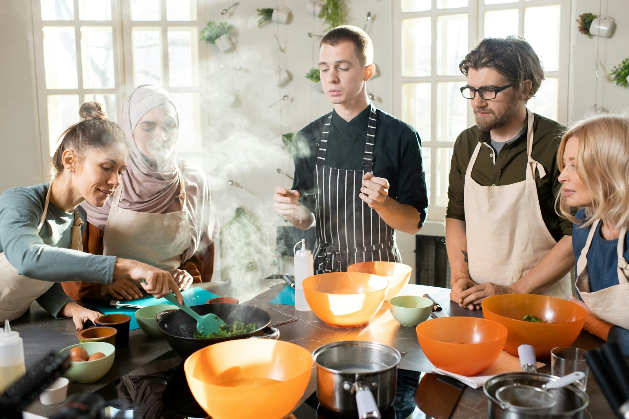 Groupe autour d'un plan de travail où l'on fait sauter des légumes verts dans un wok
