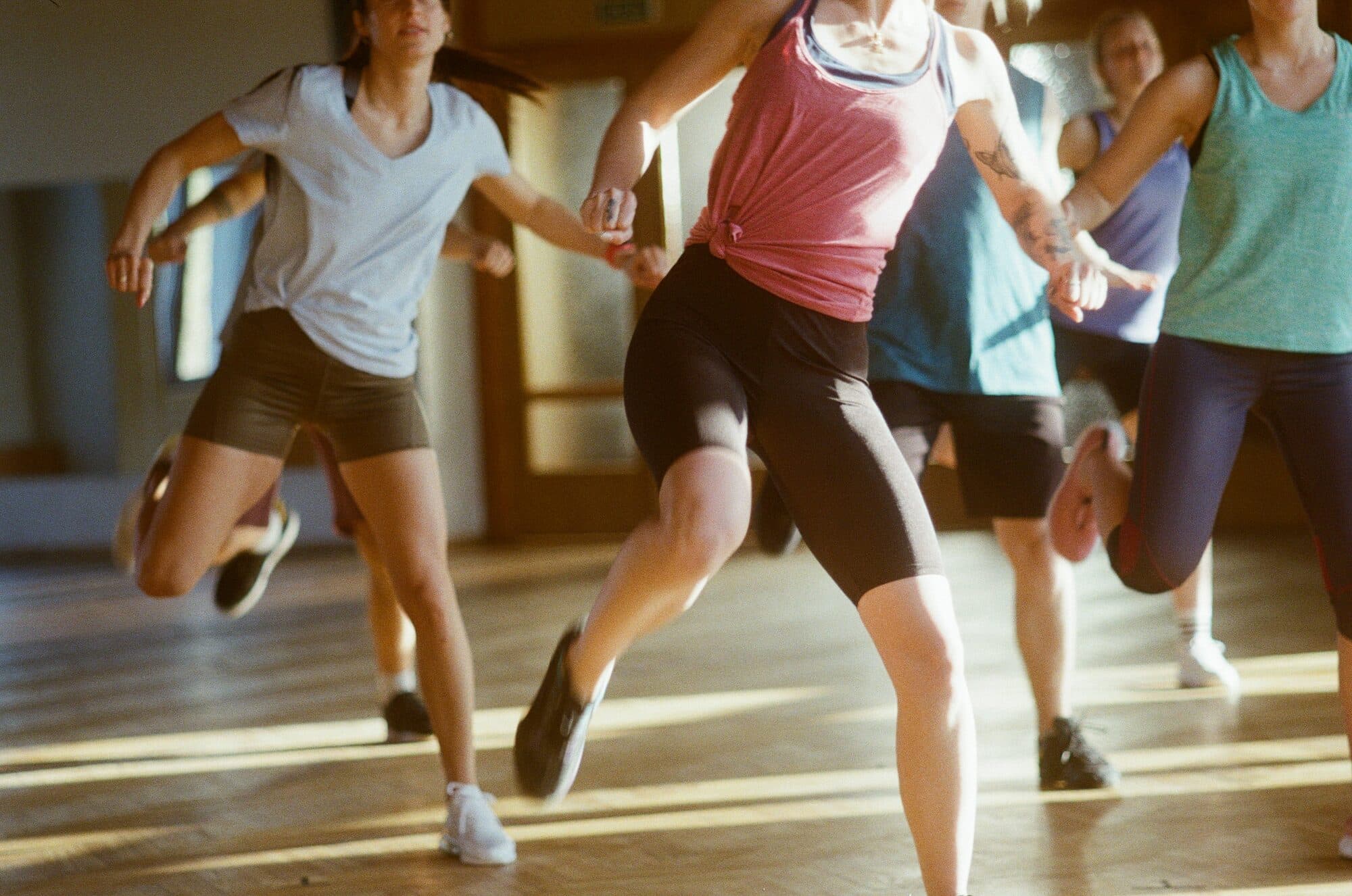 Danseurs en plein saut lors d'un cours énergique dans un studio au parquet ensoleillé