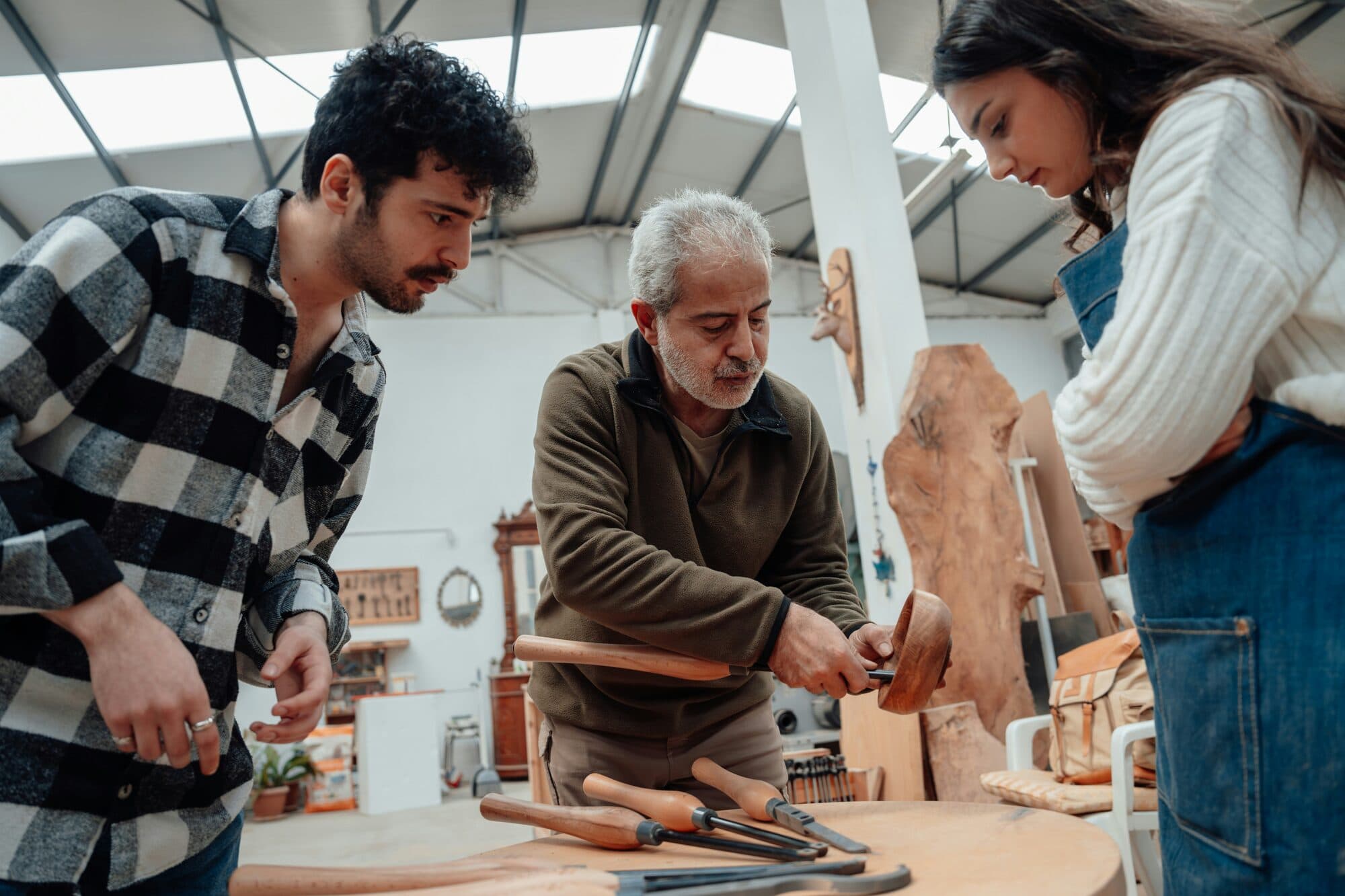 Instructeur montrant un bol en bois à deux élèves autour d'un établi d'atelier