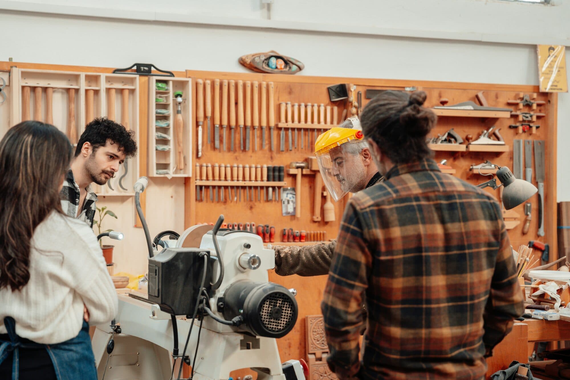 Artisan au tour à bois sous visière de protection, observé par des élèves dans l'atelier