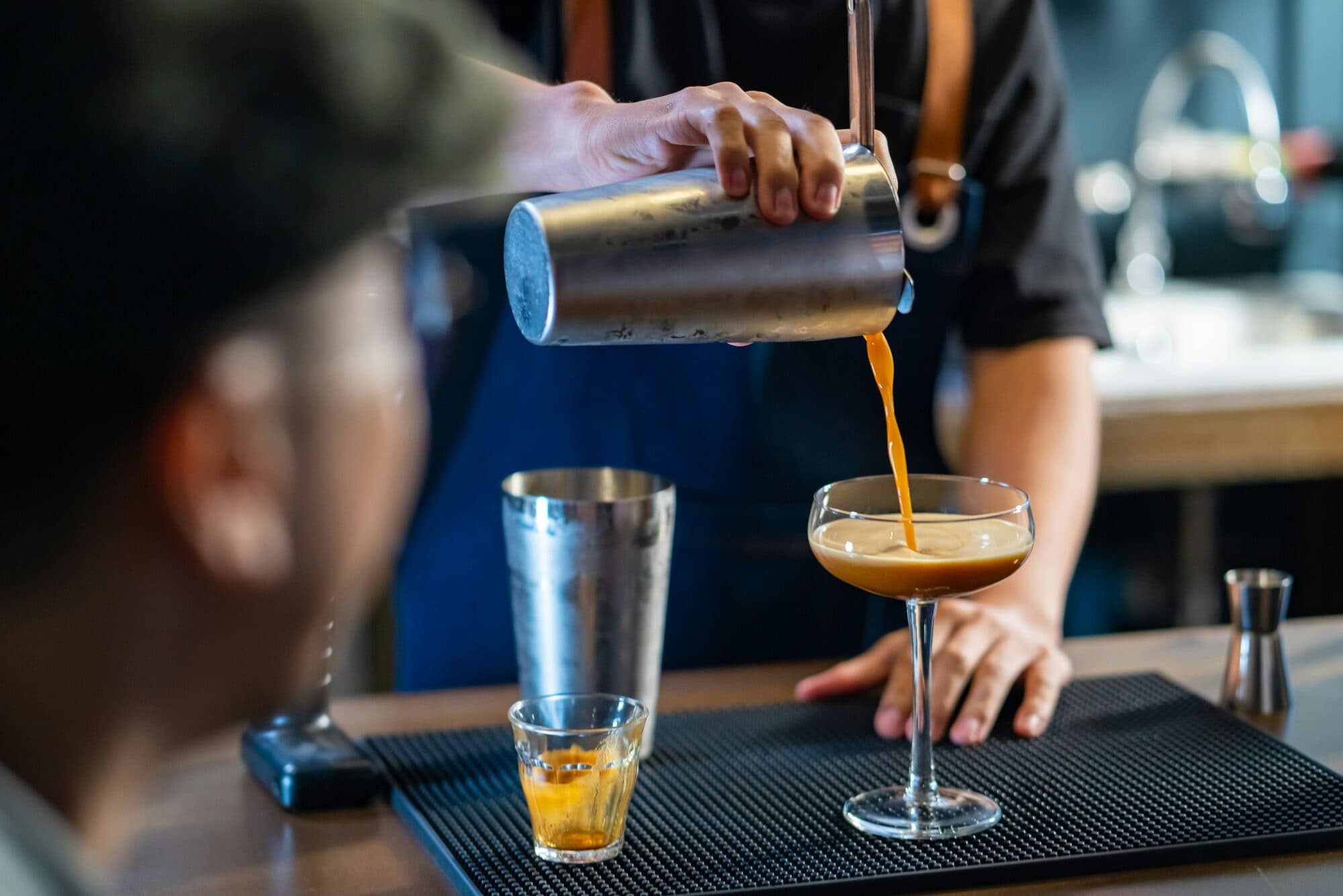 Barman versant un cocktail depuis un shaker en métal dans un verre à pied
