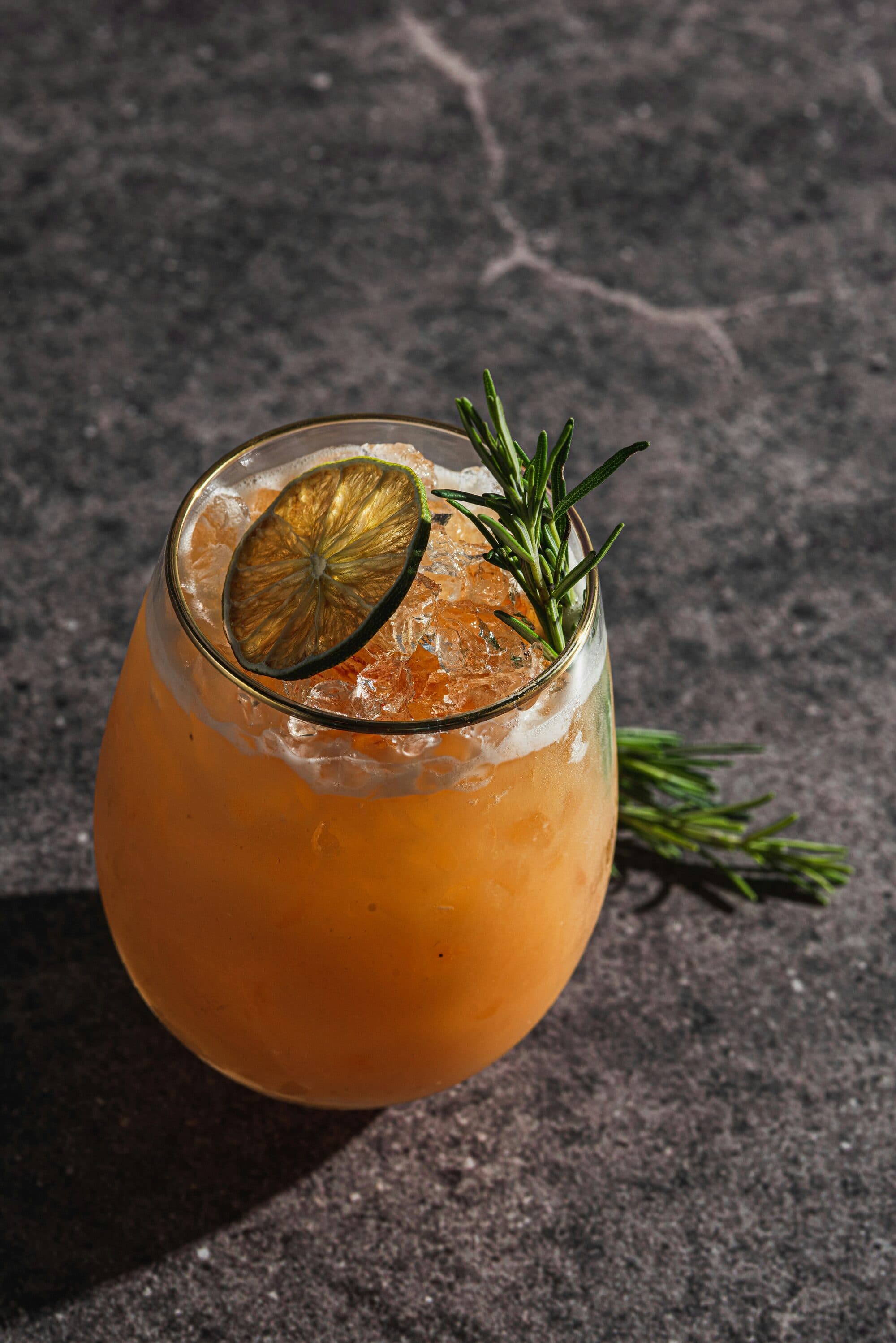 Cocktail orangé à la glace pilée garni d'une rondelle de citron vert et de romarin