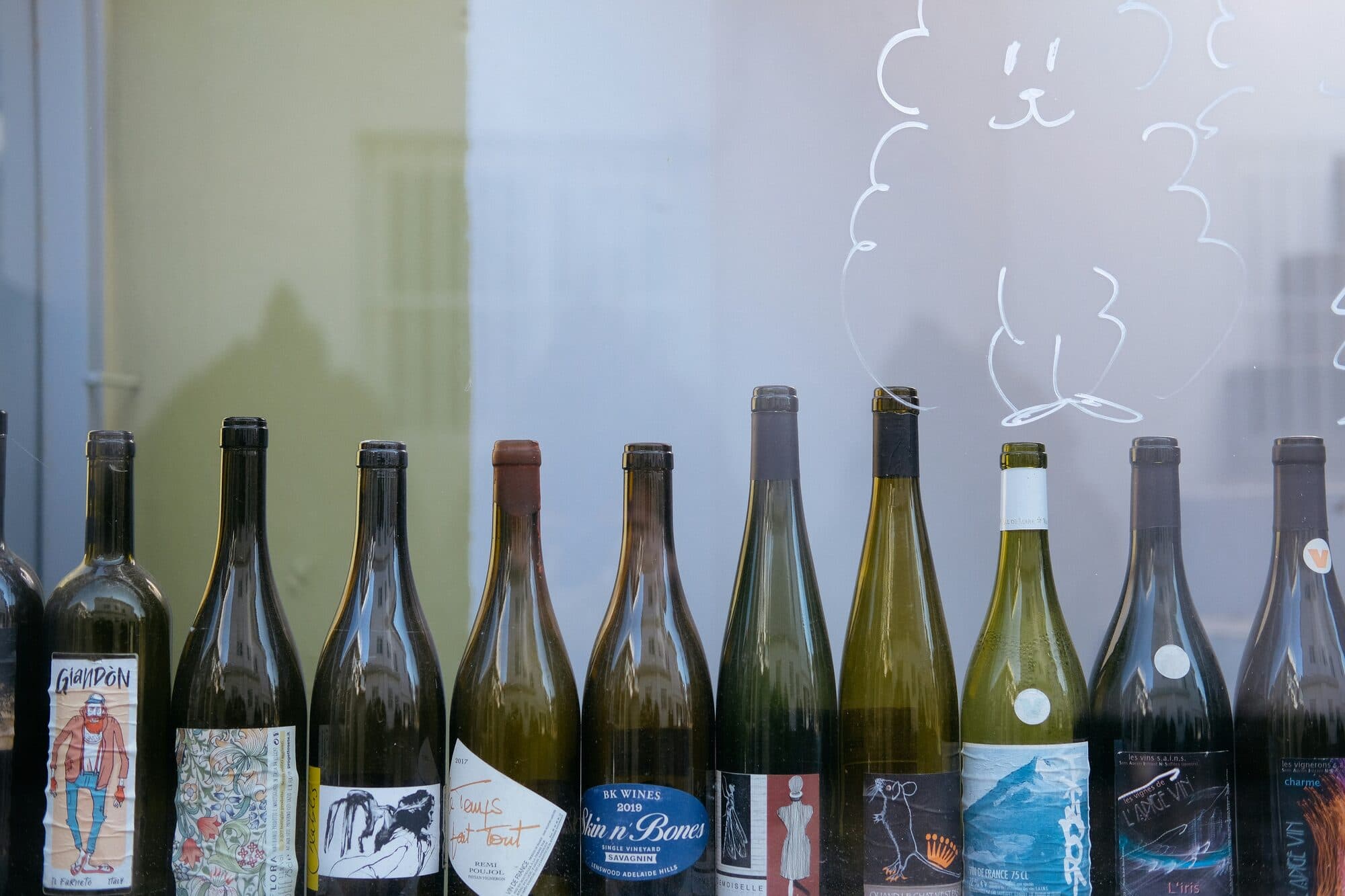 Rangée de bouteilles de vin aux étiquettes illustrées devant une vitre