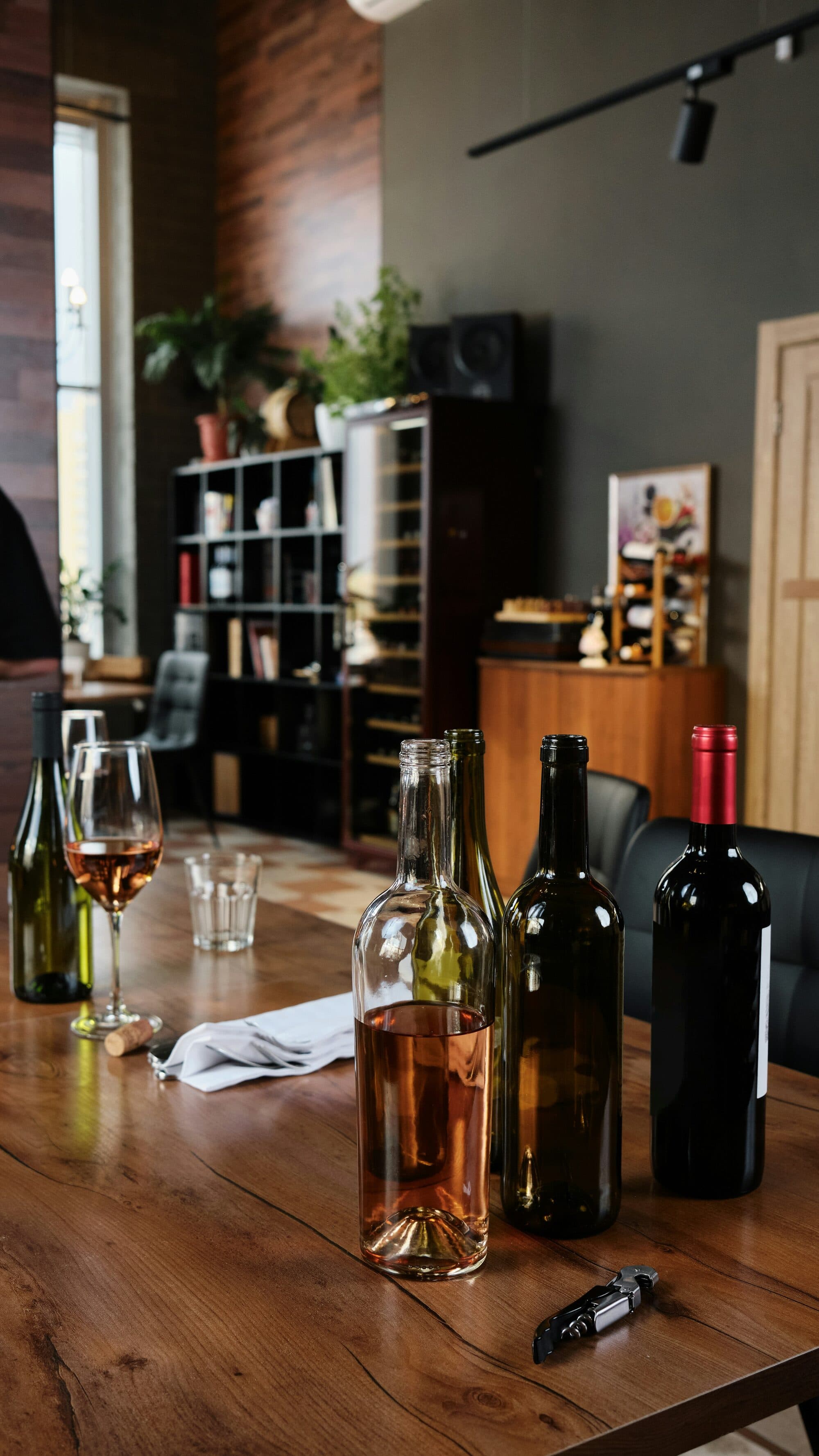 Bouteilles de vin, verre de rosé et tire-bouchon posés sur une table en bois