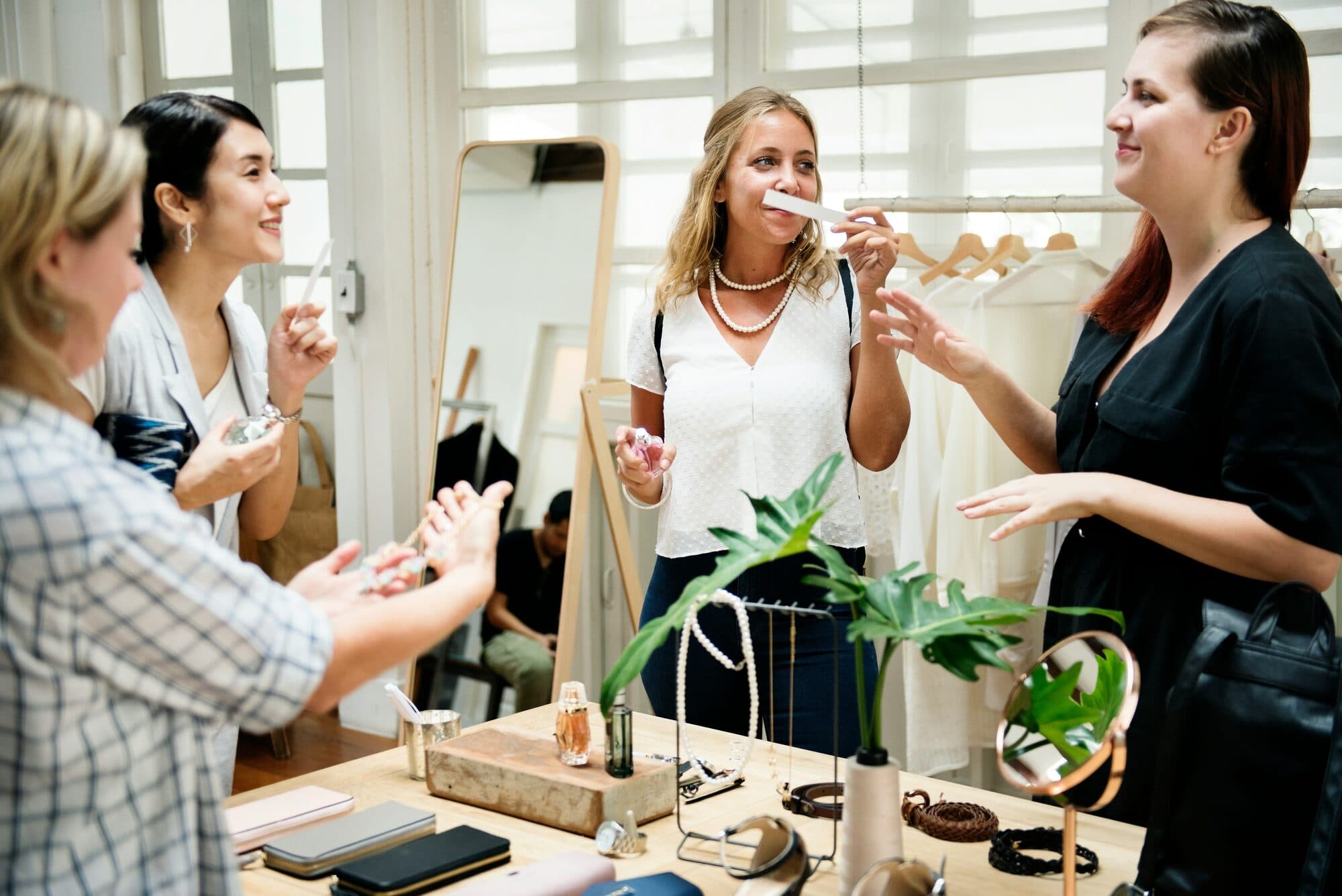Femmes sentant des bandes de papier autour d'une table garnie de flacons de parfum