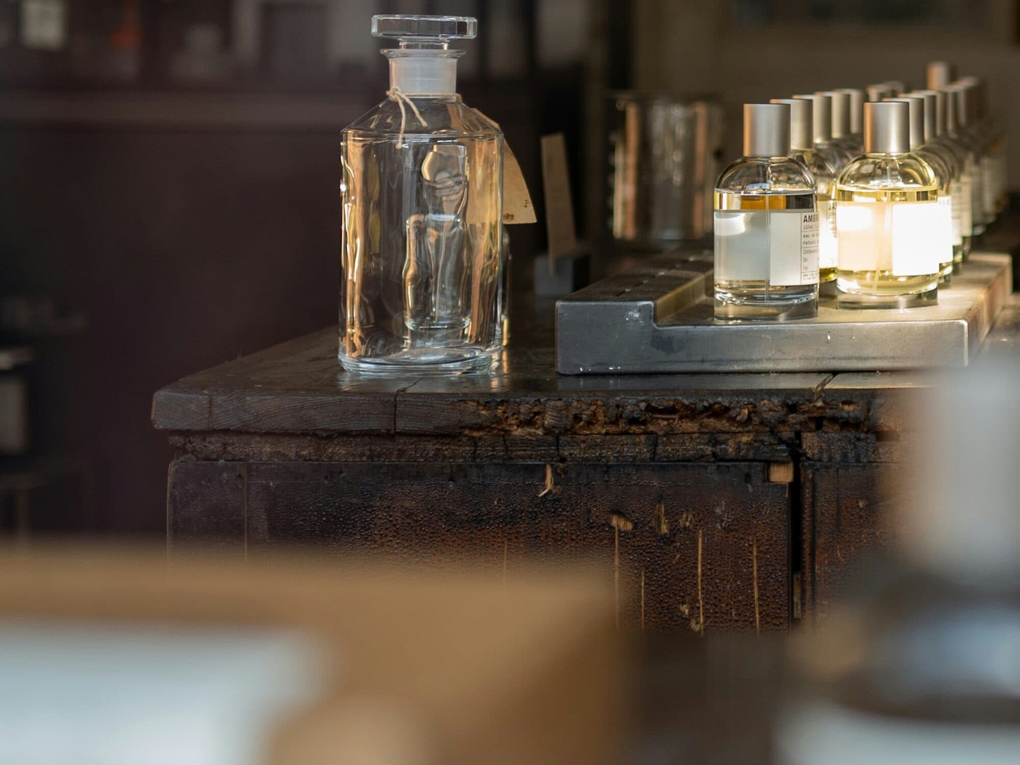 Grand flacon de verre et rangée de flacons de parfum dorés sur un comptoir en bois