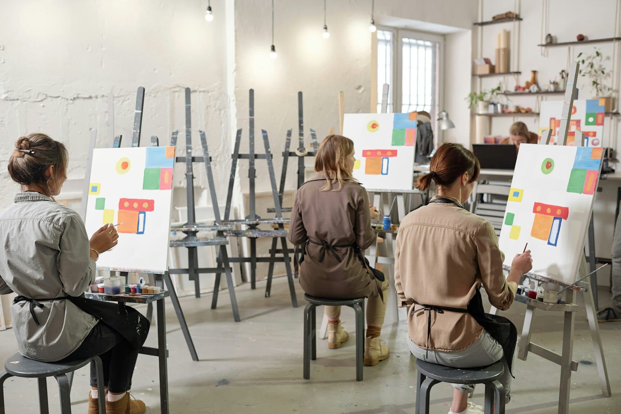 Trois participantes peignant la même composition colorée sur des chevalets dans un atelier