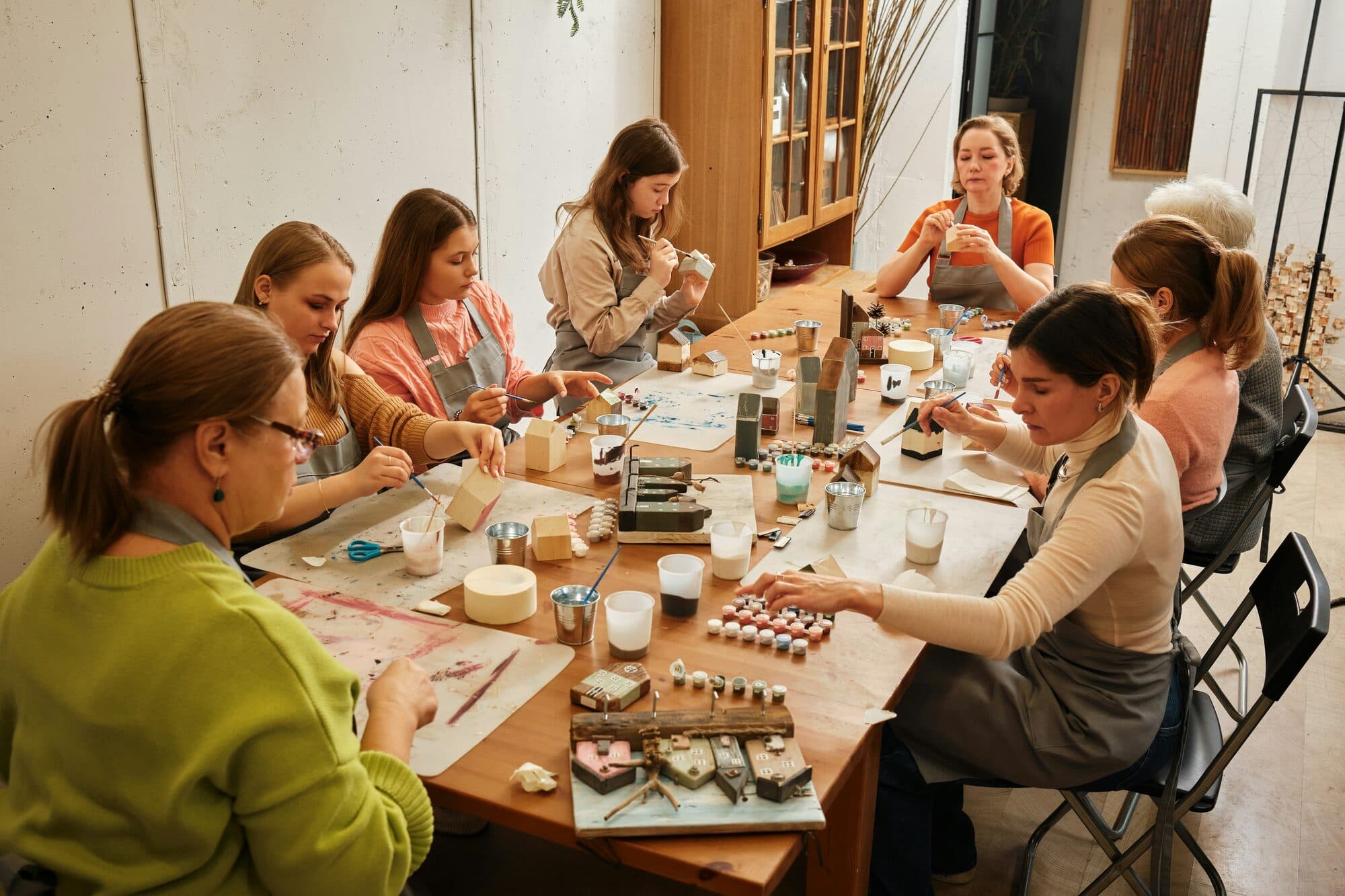 Femmes et enfants peignant de petites maisons en bois autour d'une table d'atelier
