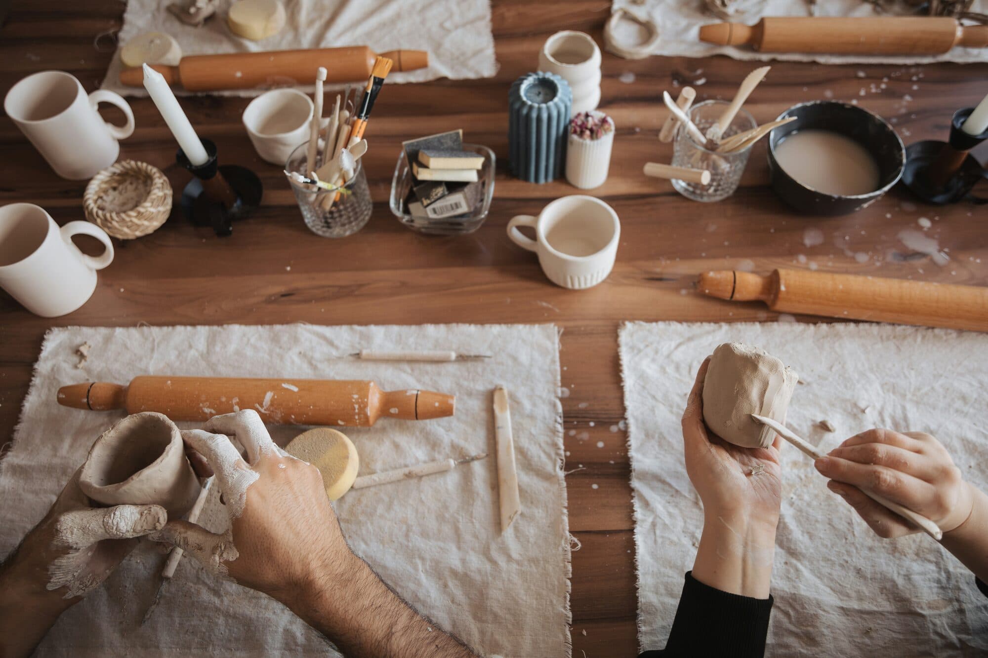 Mains façonnant de l'argile claire sur un établi en bois parmi outils et tasses en céramique