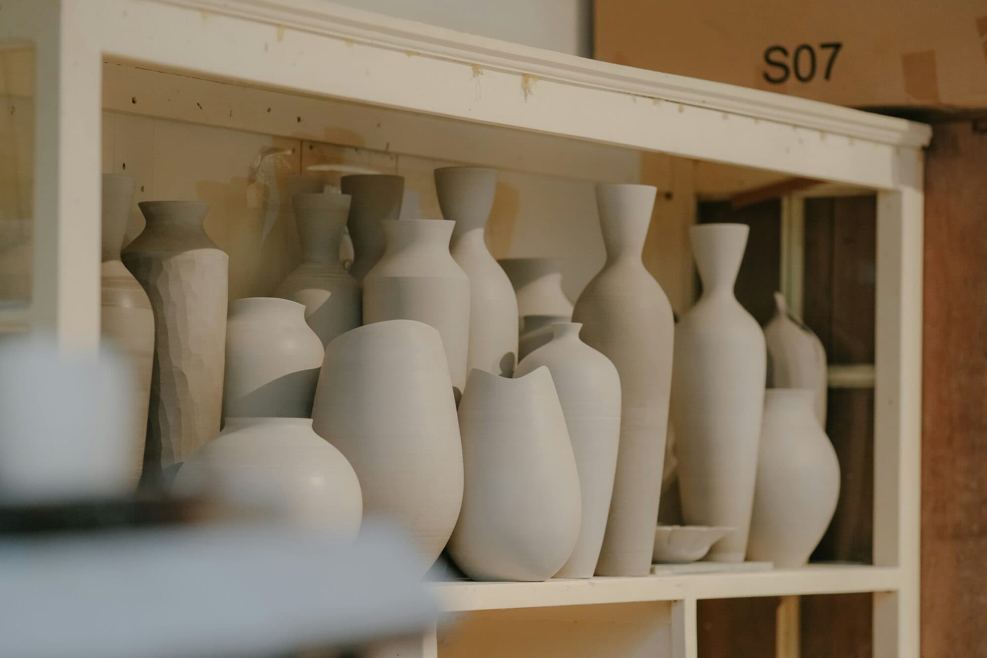 Pièces de poterie en argile brute aux formes variées alignées sur une étagère blanche