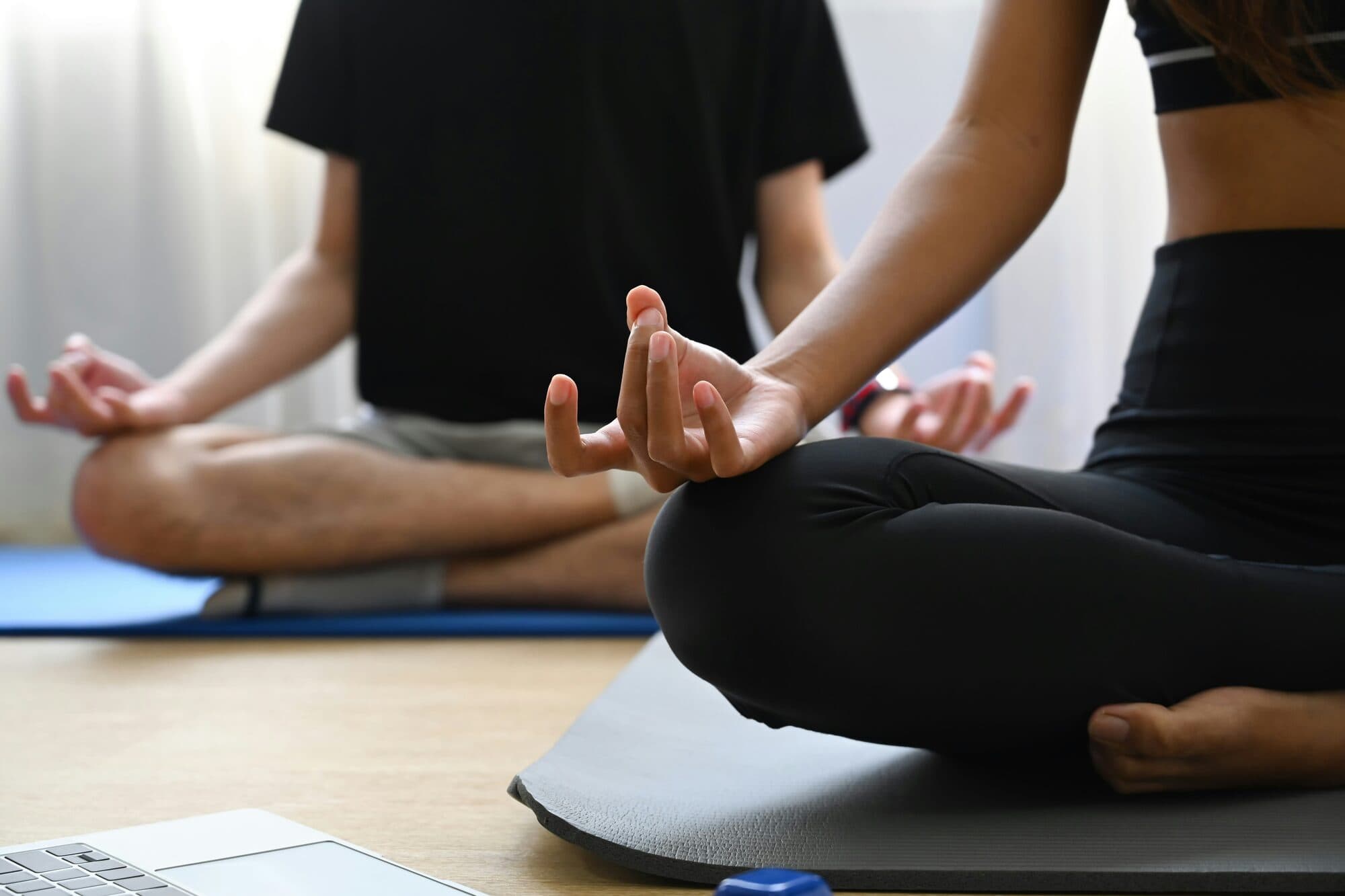 Homme et femme assis en méditation sur des tapis de yoga près d'un ordinateur portable