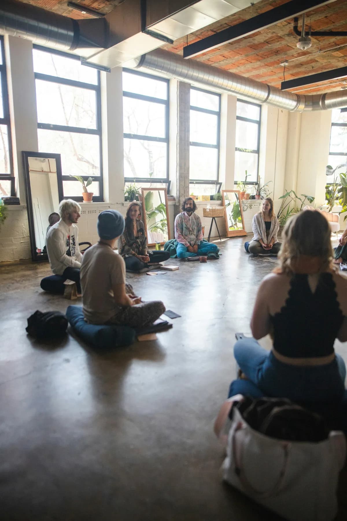 Groupe assis en cercle sur des coussins, dans une salle lumineuse, pendant un cours de yoga