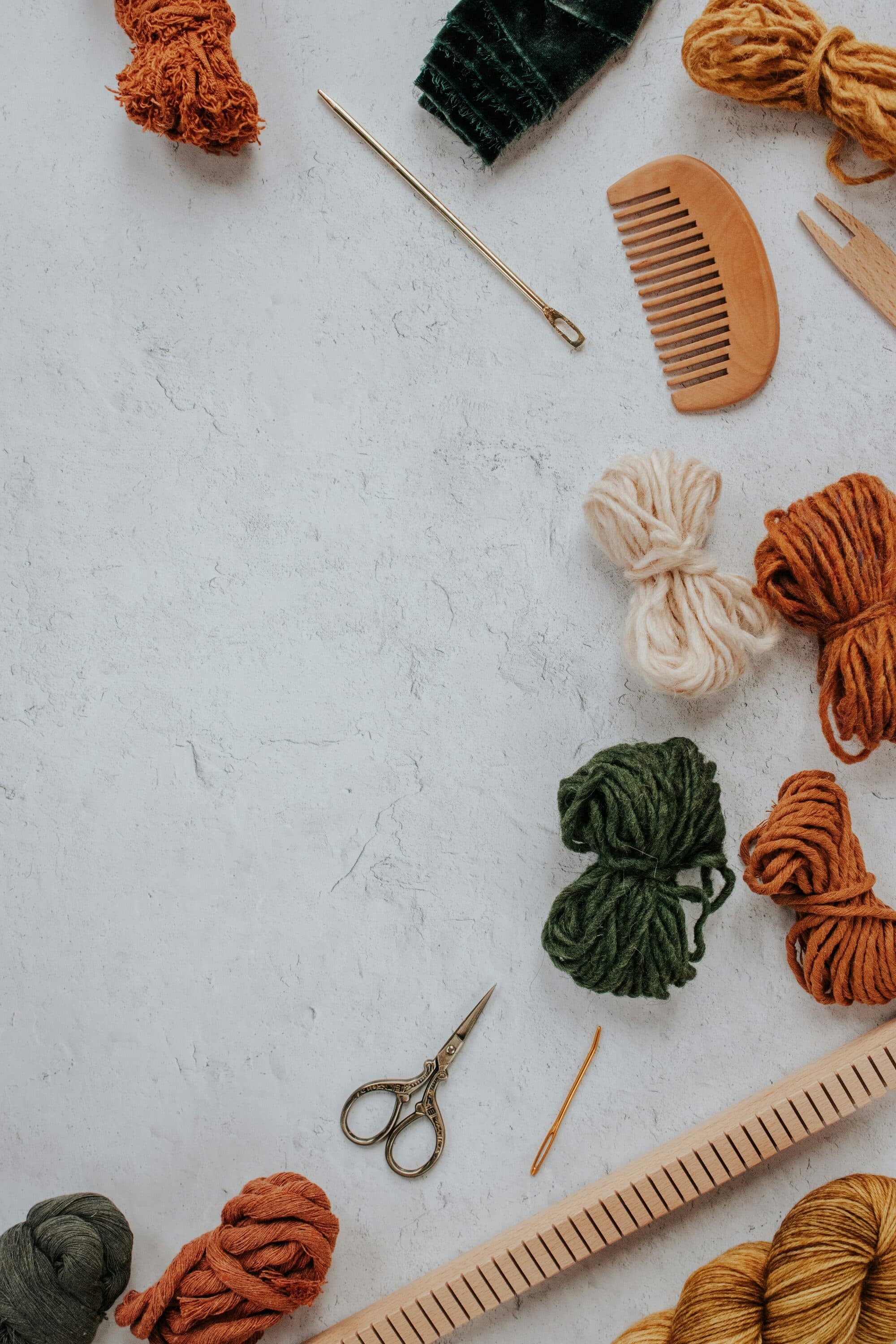 Pelotes de laine colorées, peigne en bois et ciseaux posés sur une surface claire